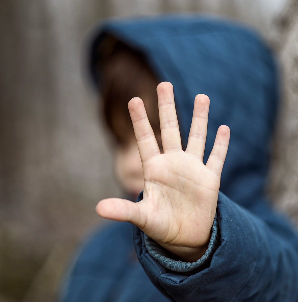 Child in blue hoodie holding up his hand