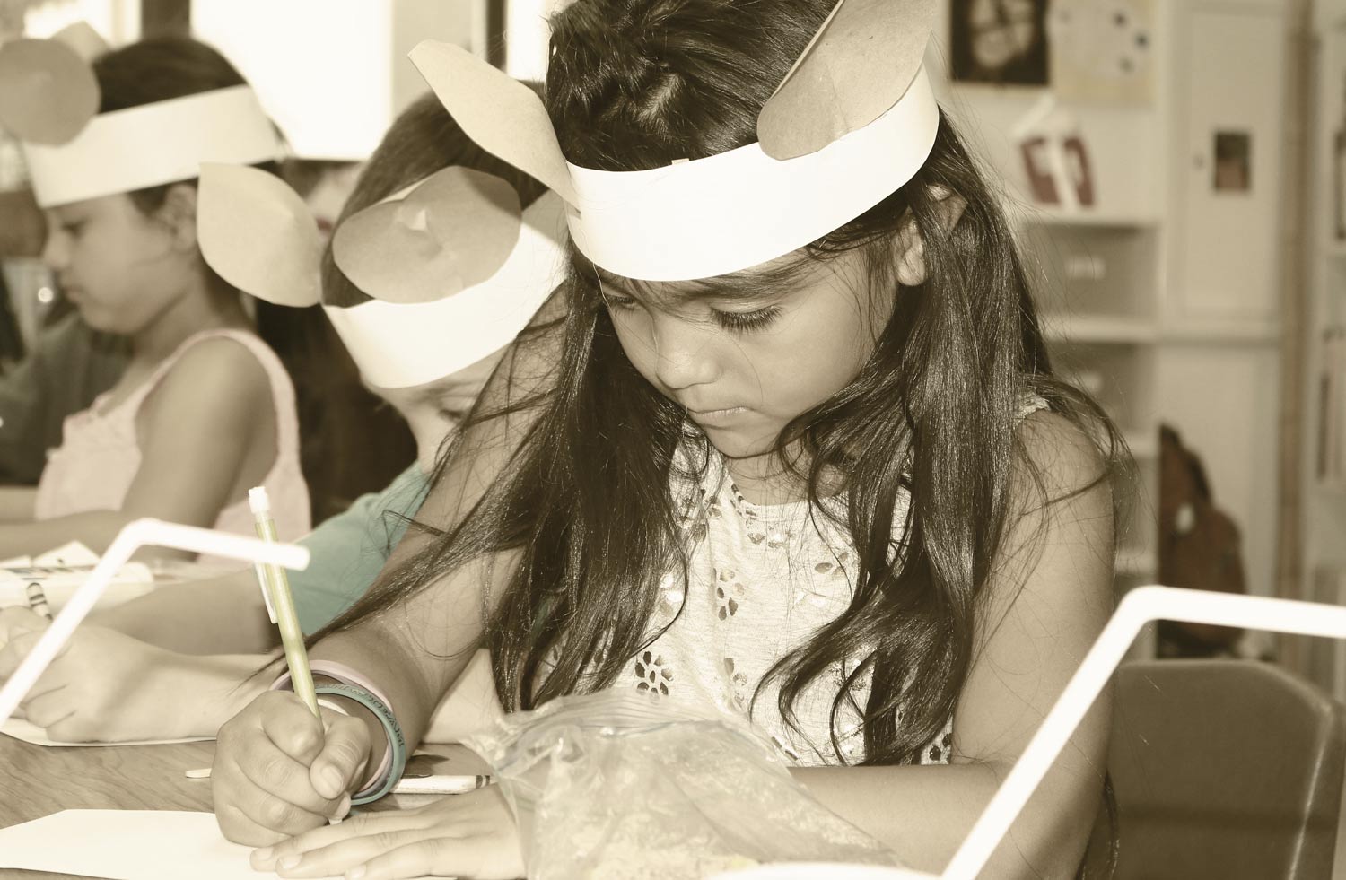 Little Girl Wearing Paper Bunny Ears and Drawing in Classroom 