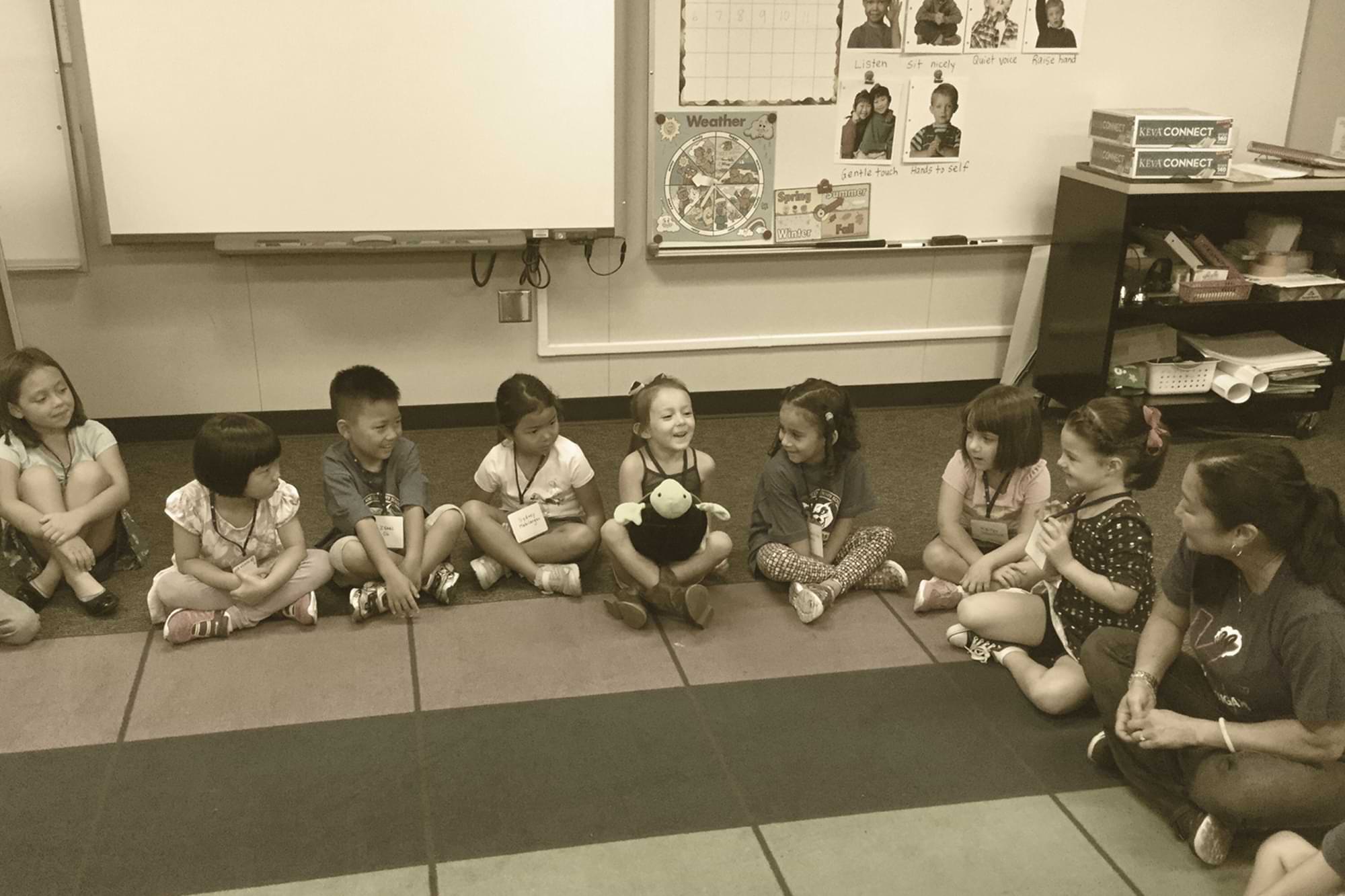 Elementary class sitting in a circle on rainbow carpet