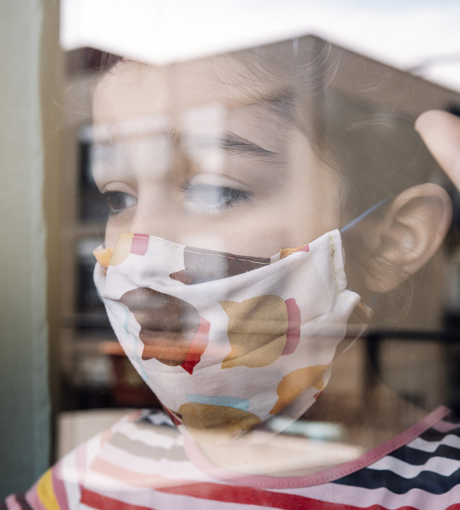 girl staring out window wearing medical mask