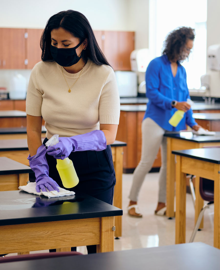 Two women cleaning desks in a school