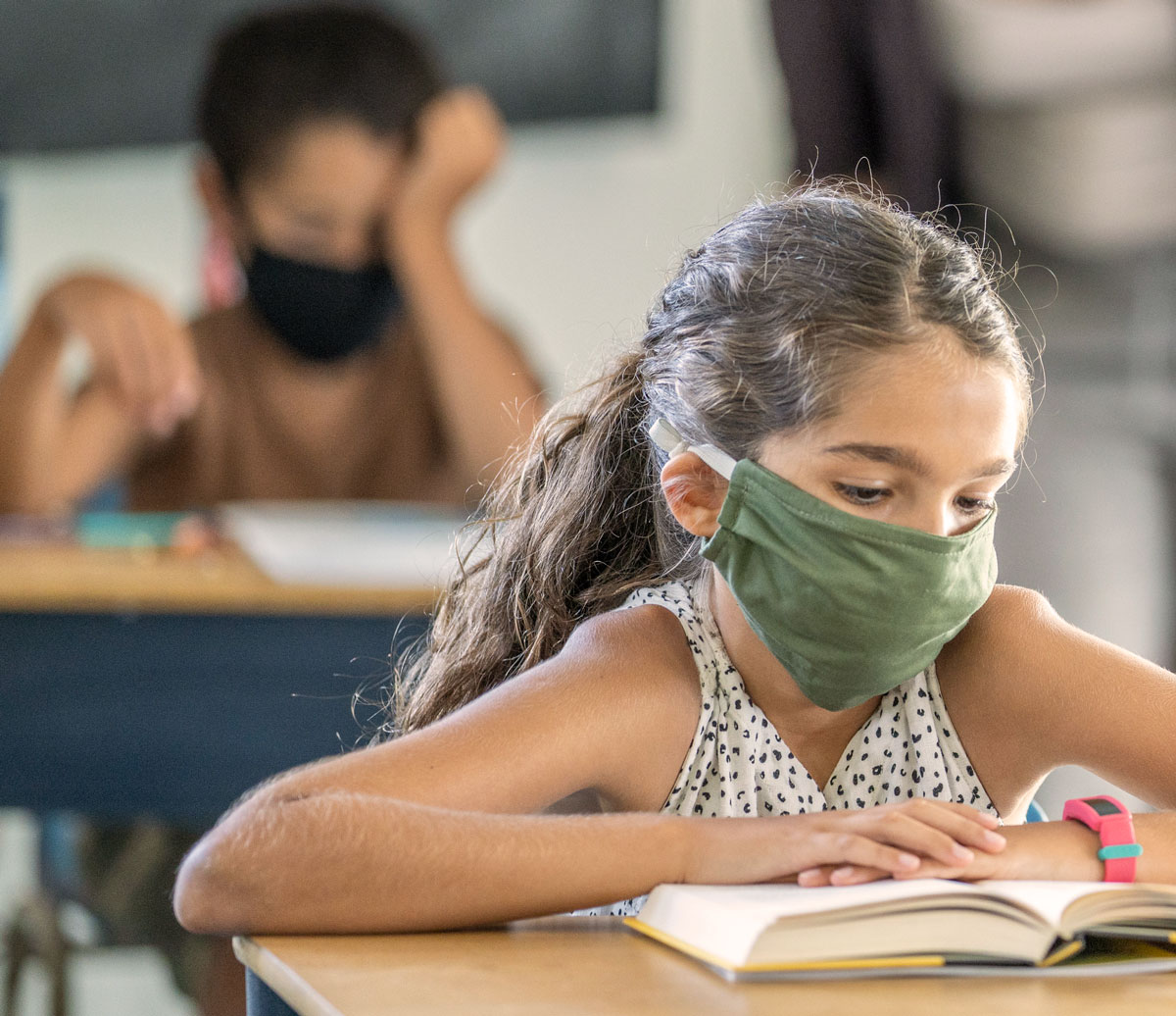 Young girl wearing a mask and reading book in classroom