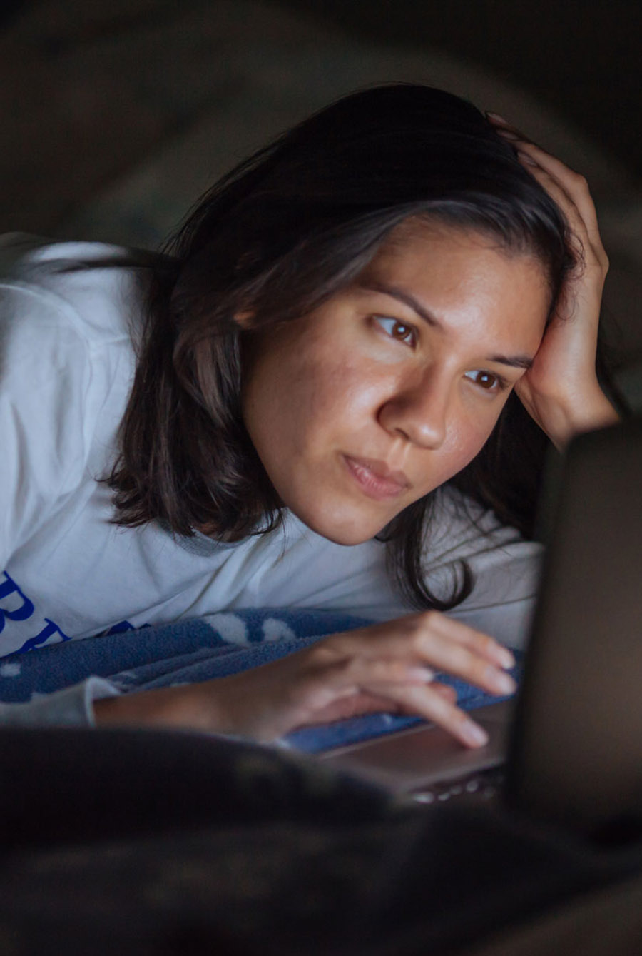 Person leaning on their elbow and using a laptop in bed in a dark room