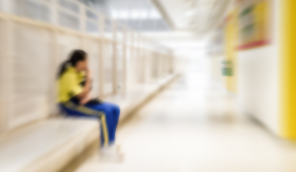 Zoom blurred photo of a girl on her phone, alone in a brightly lit hallway of a school