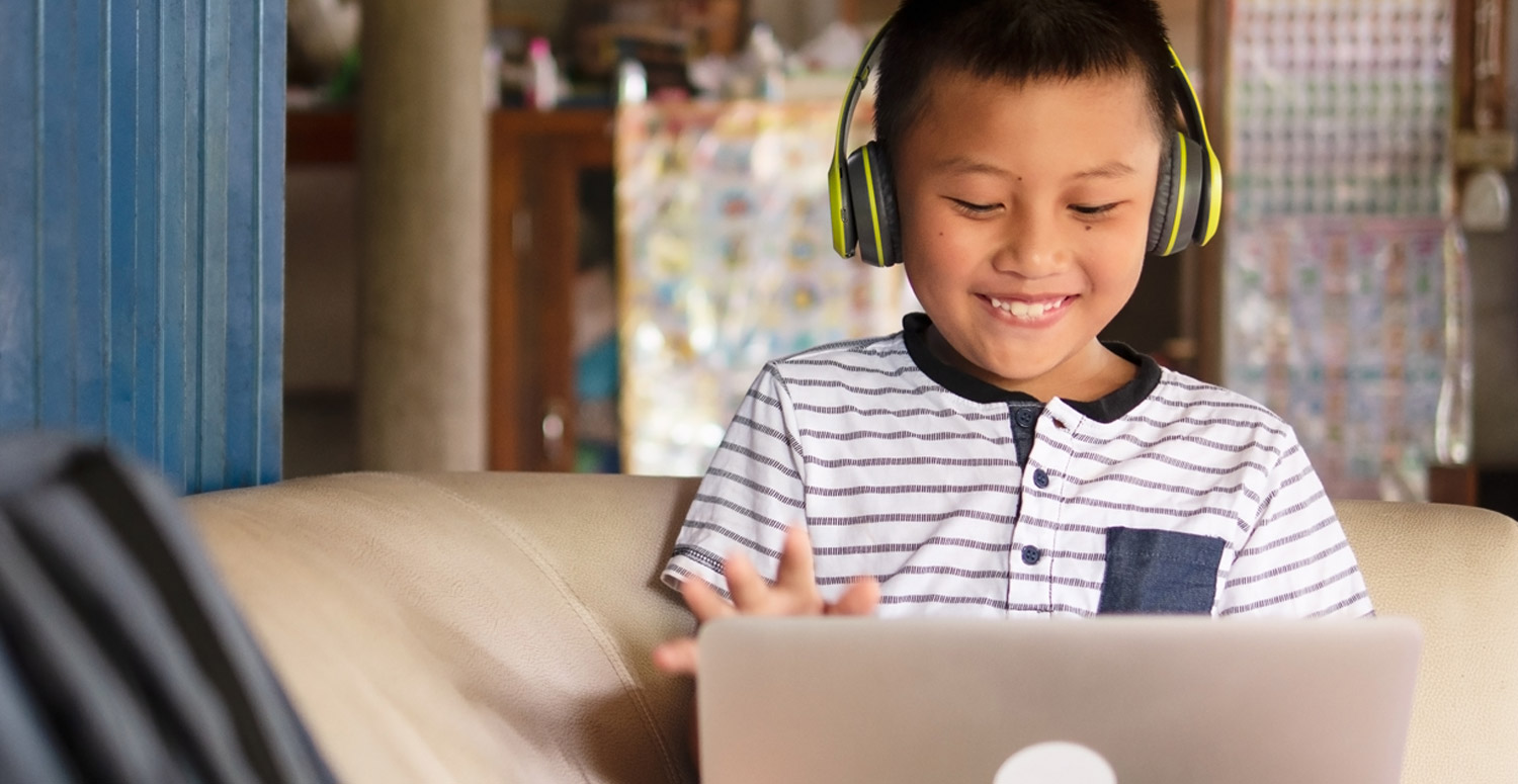 child wearing headphones smiles while on a laptop