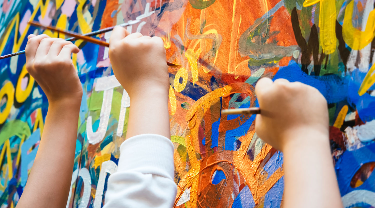 Three children's hands painting a colorful wall mural with paint brushes