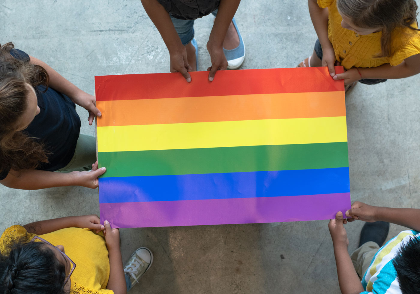 A group of five students holding up a colorful pride flag above a concrete floor