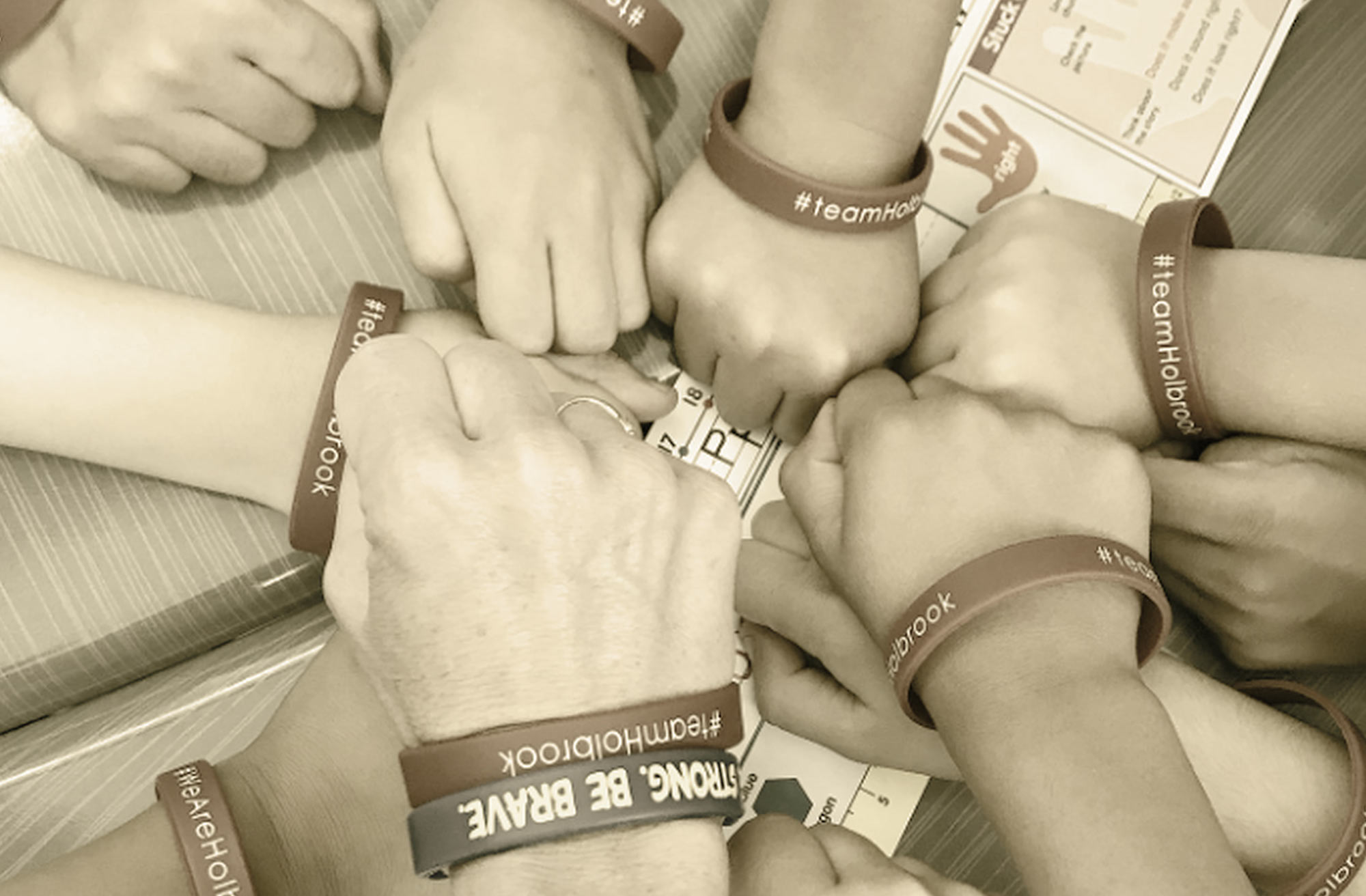 a huddle of students hands including an adult, all wearing #teamHolbrook bracelet