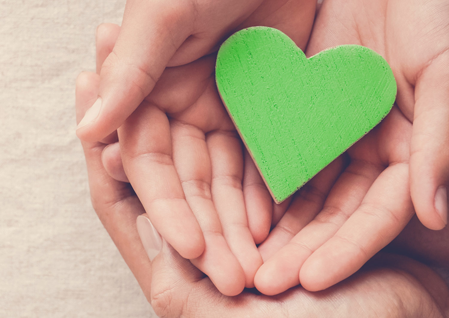 child and adult hands together, holding a green heart
