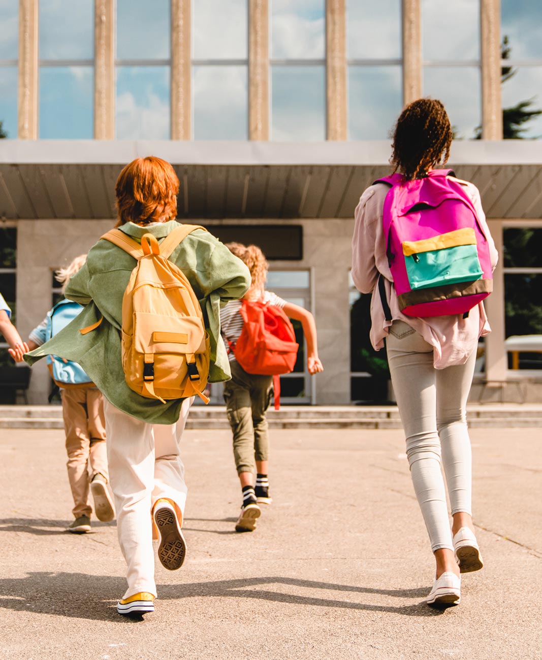 children wearing back packs run towards a school entrance