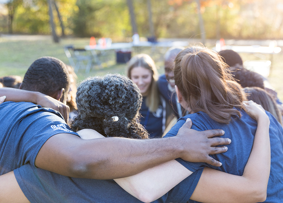 A group of individuals all hug together outside while smiling with their arms around each other