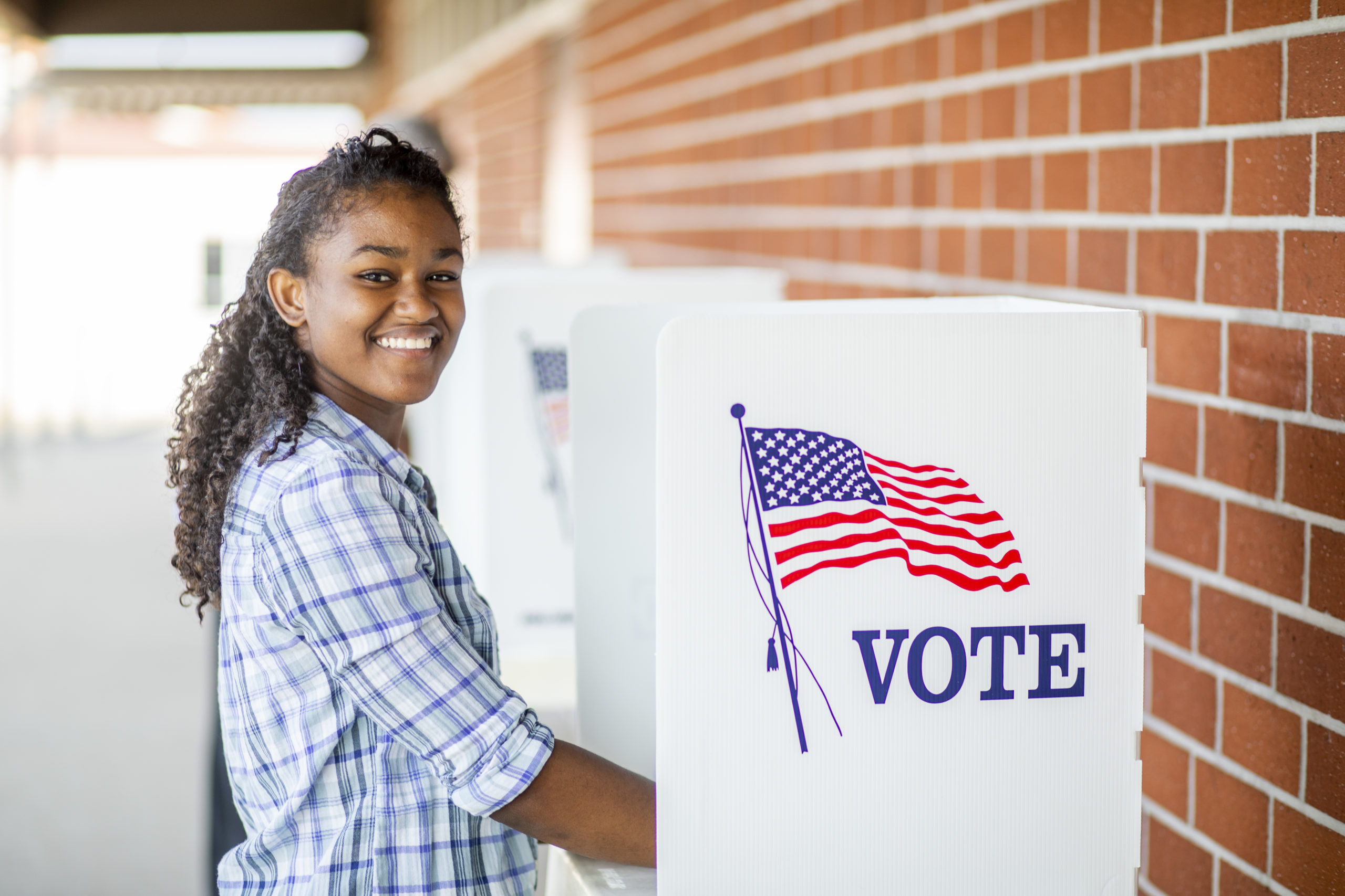 a young student stands smiling at a voting box