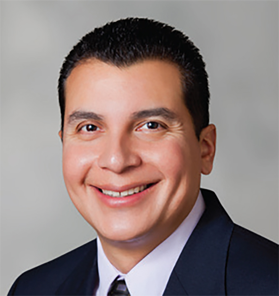 A portrait headshot photographic perspective of Albert Gonzalez smiling in a suit and tie