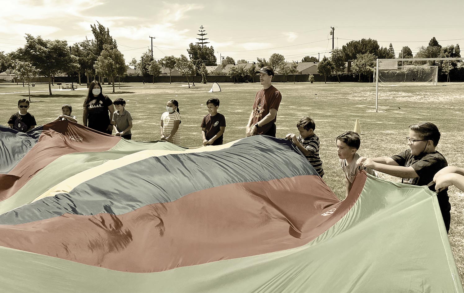 Kids and School Leaders playing a game with a giant rainbow tarp in a soccer field