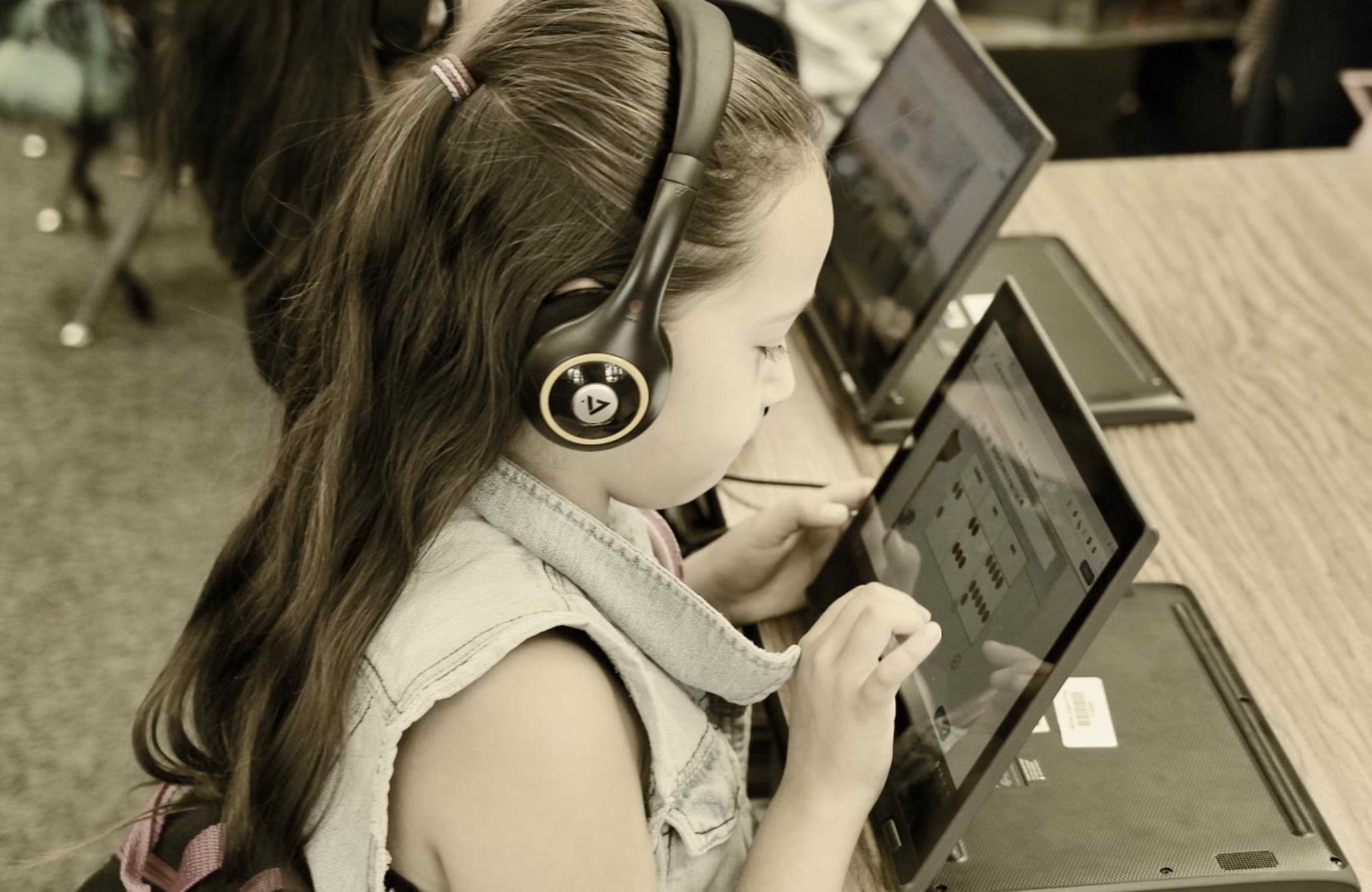 an elementary aged student sits at a desk wearing headphones and using a tablet to study math