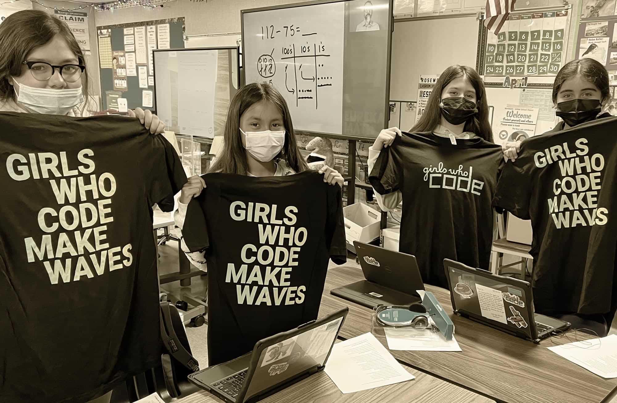 masked middle school aged female students hold shirts that read "Girls who code make waves"