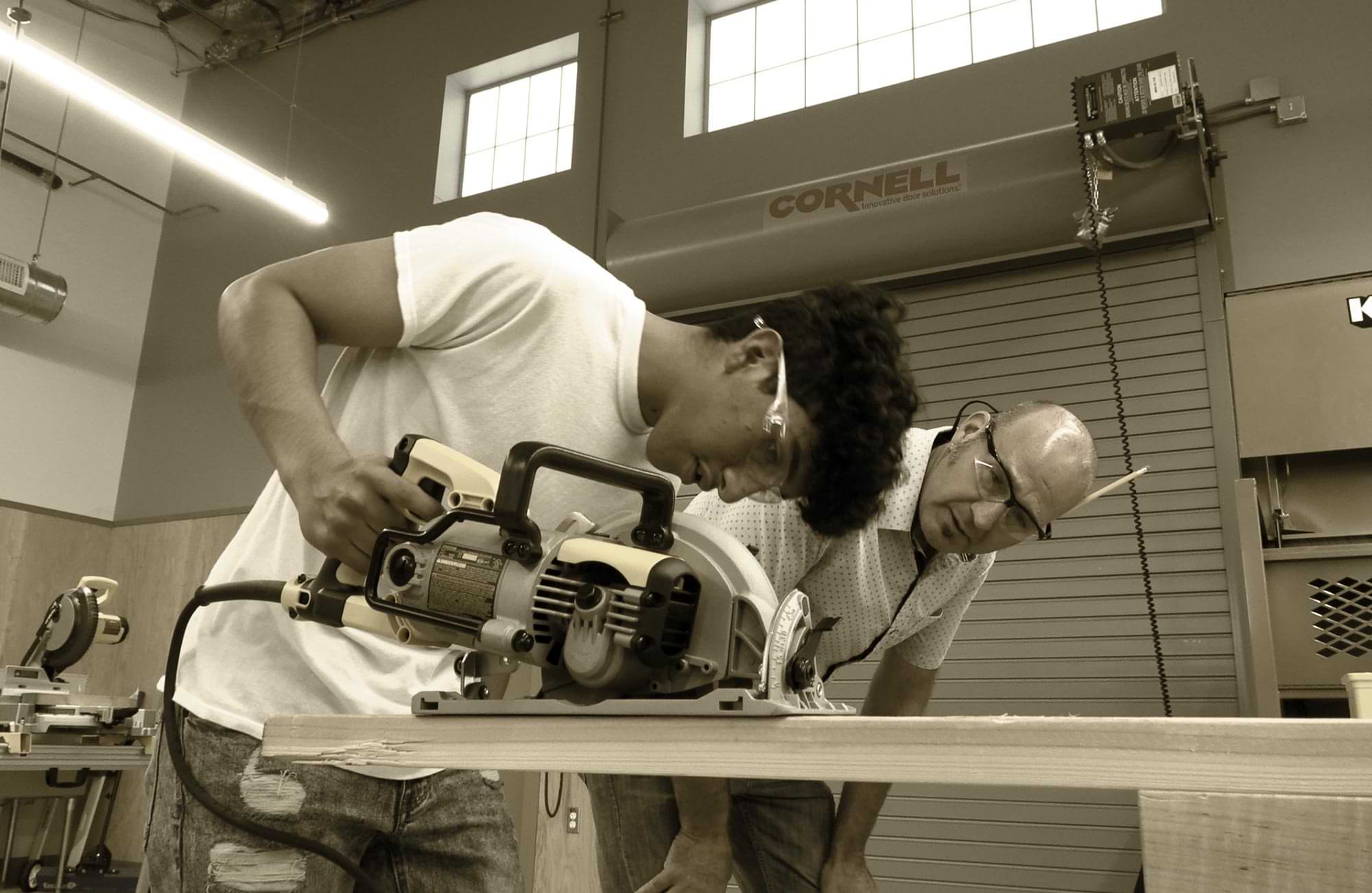 a student is supervised while cutting a piece of wood with a power tool