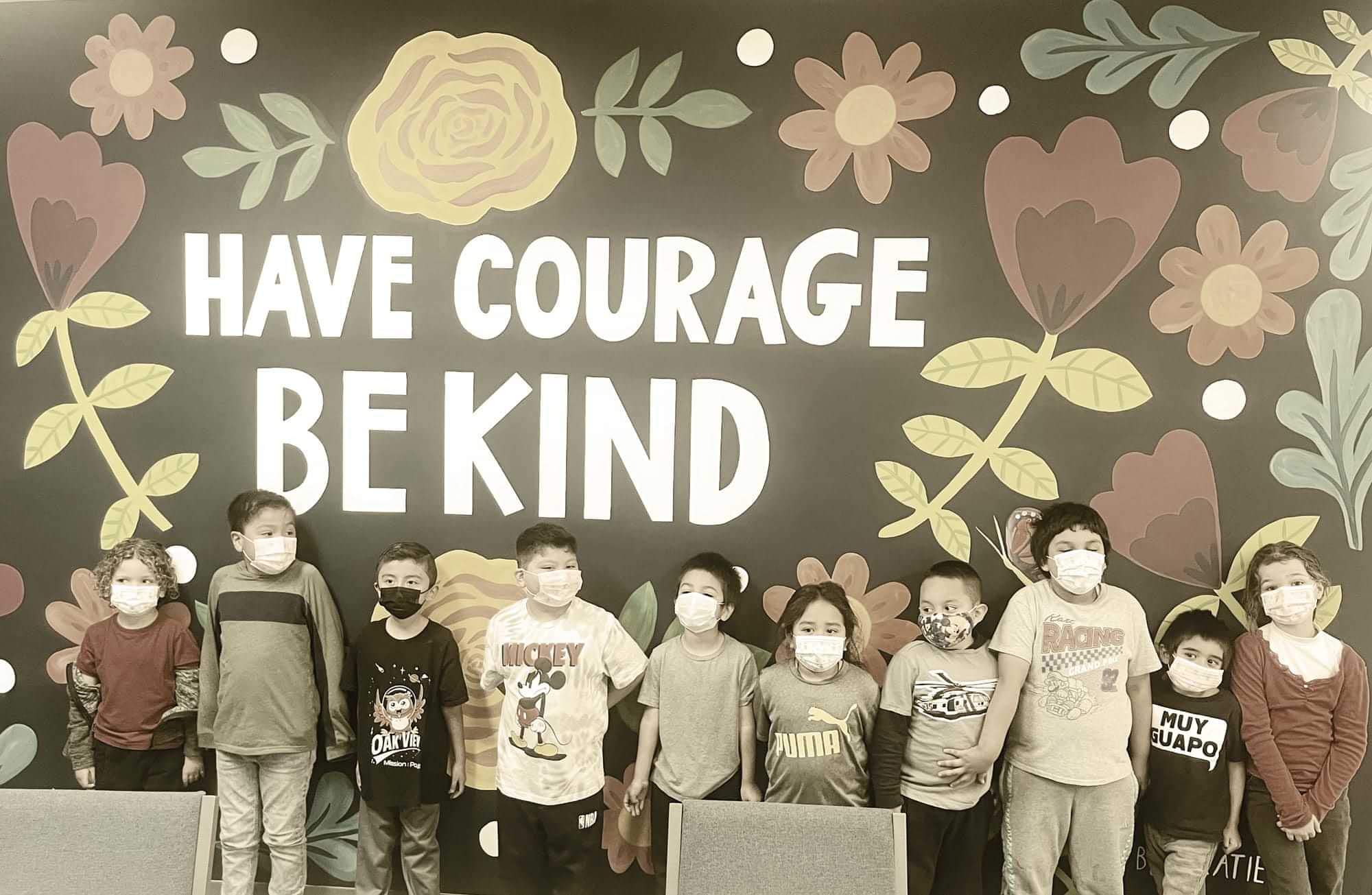 elementary aged students stand up against a wall that reads "Have courage, Be kind"