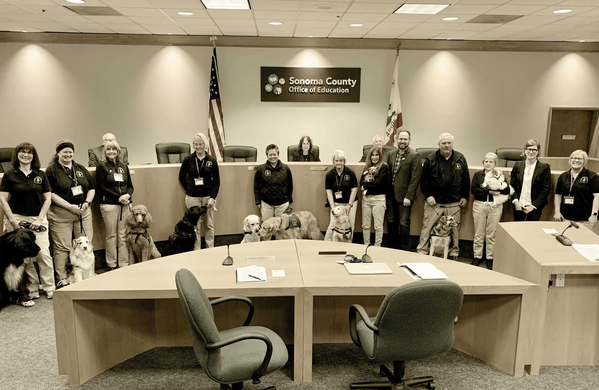emotional support dogs and their attendants stand at the head of a conference room for a group photo