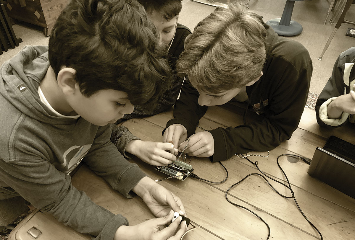 Three elementary students working on a PCB