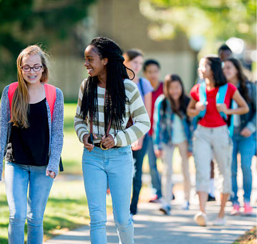 Two girls walking on the sidewalk with students walking behind them 