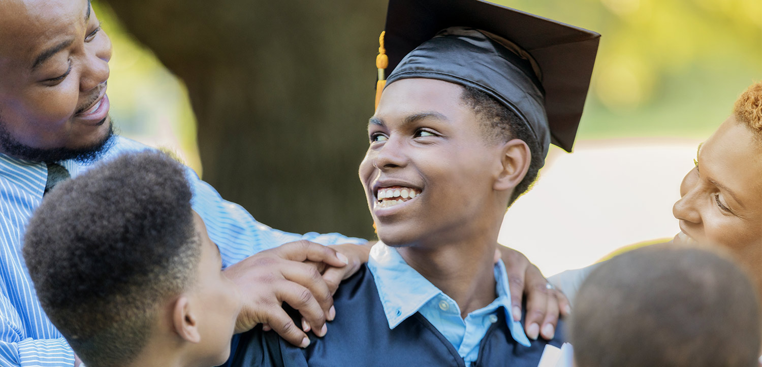 a young black student wears a grad cap surrounded by his smiling family members