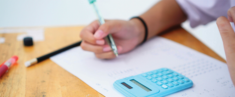 Student filling in test with a blue calculator on the desk.