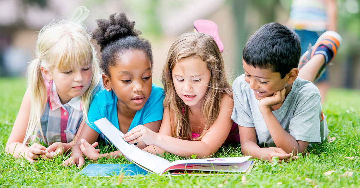 four children laying on the grass next to each other reading a book