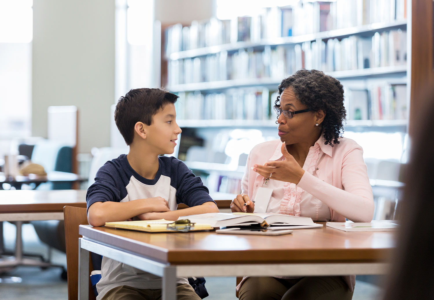 a young boy and woman do work together at a library study table
