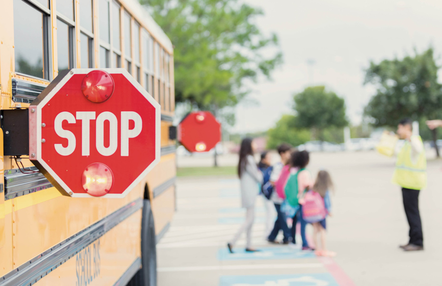 stop sign on a school bus with a crossing guard helping students cross the street