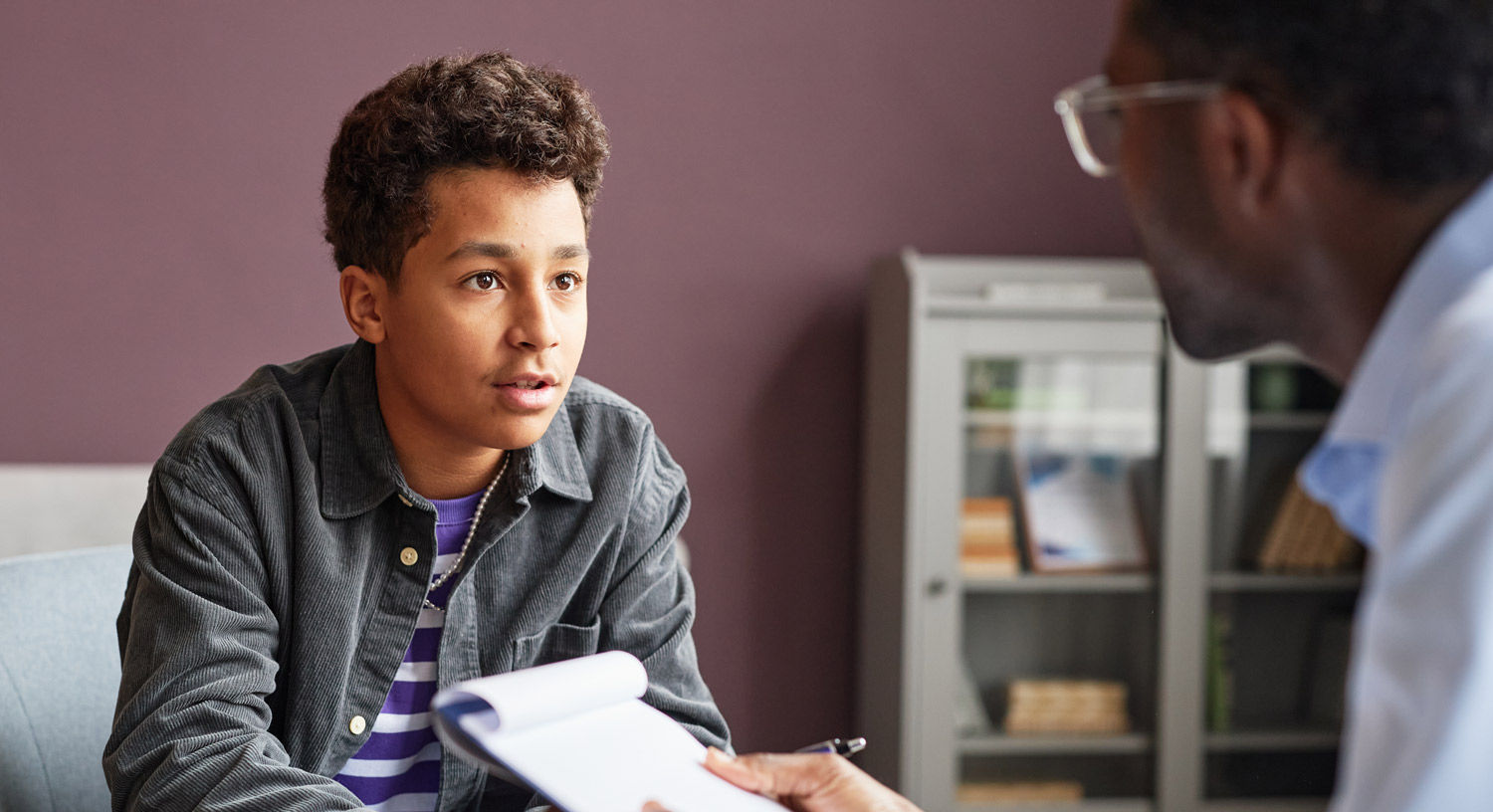 a teenaged boy speaks with a counselor in an office
