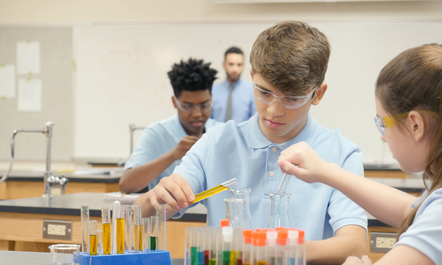 secondary school aged kids pour liquids into scientific flasks in a lab classroom