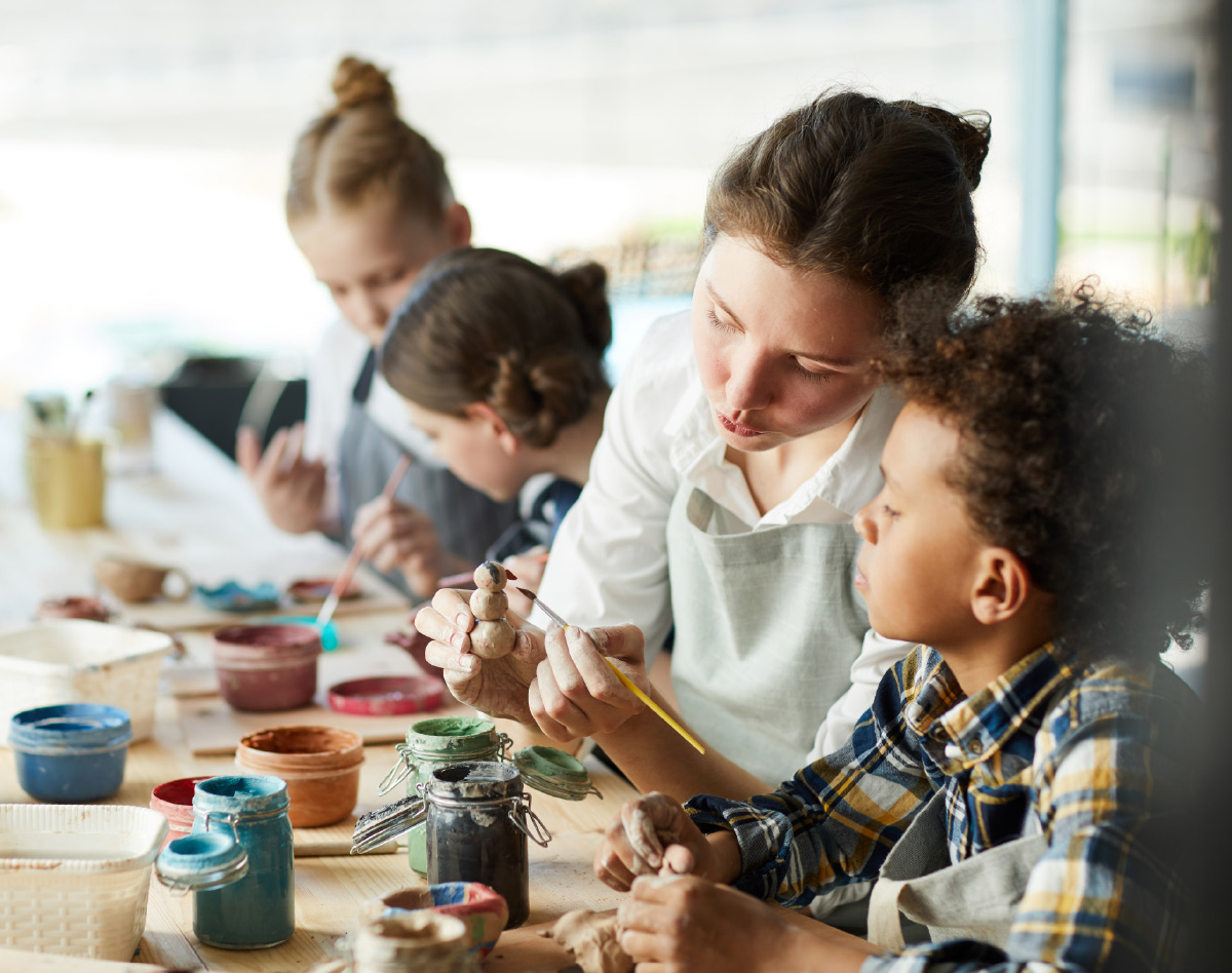 women showing young children how to paint at craft table