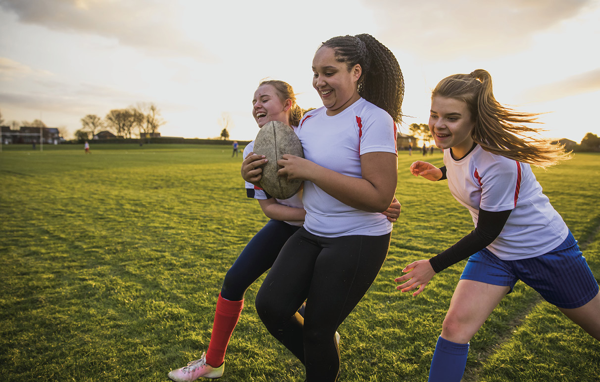 3 girls smile as they play flag football with each other