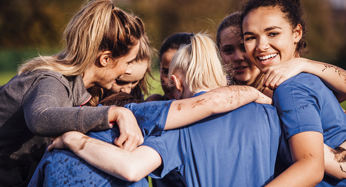 girls smile in a huddle with mud on their arms from flag football