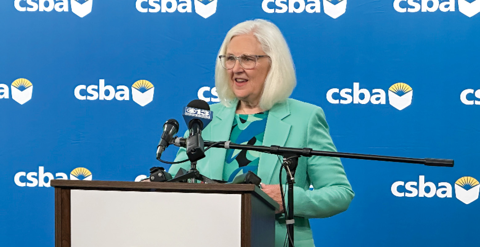 CSBA President Susan Markarian wearing glasses and a teal balzer and blouse, speaks into the podium microphone during a June 26 press conference