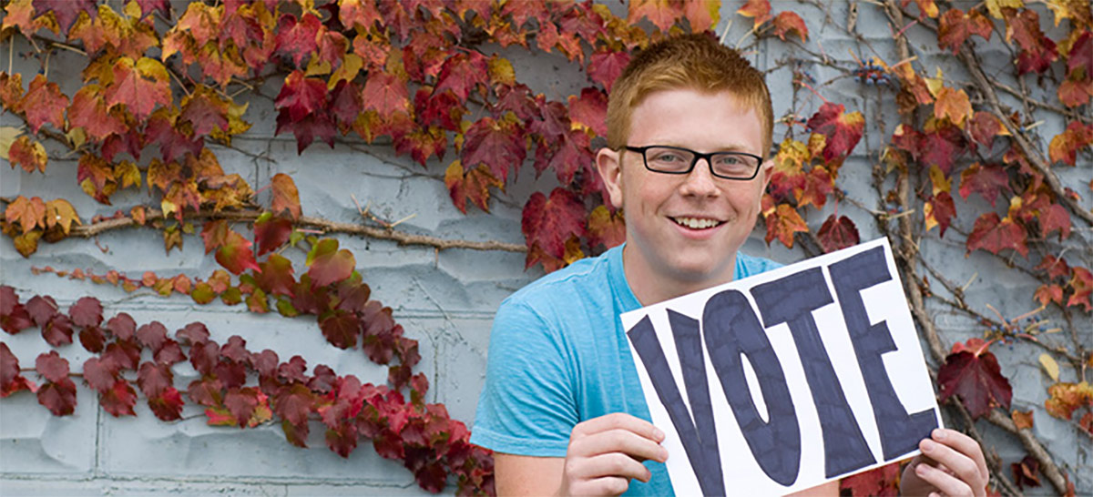 smiling student holding up a sign that reads "VOTE"