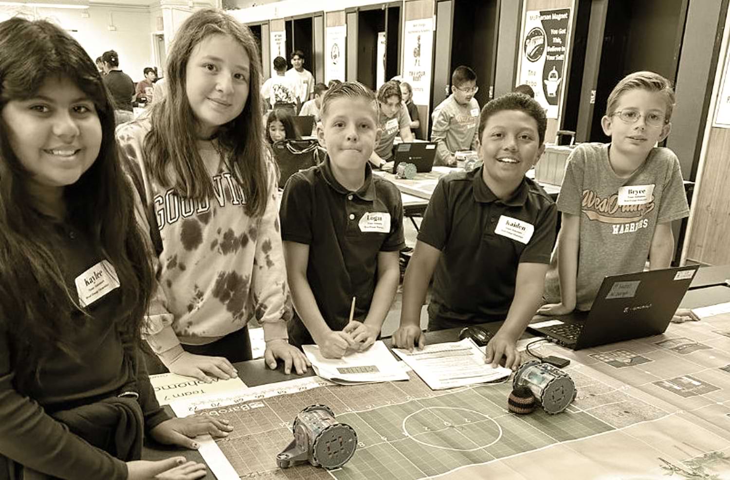 five elementary aged students from West Orange Mathematics Academy smile for a group photo at a STEM event team table