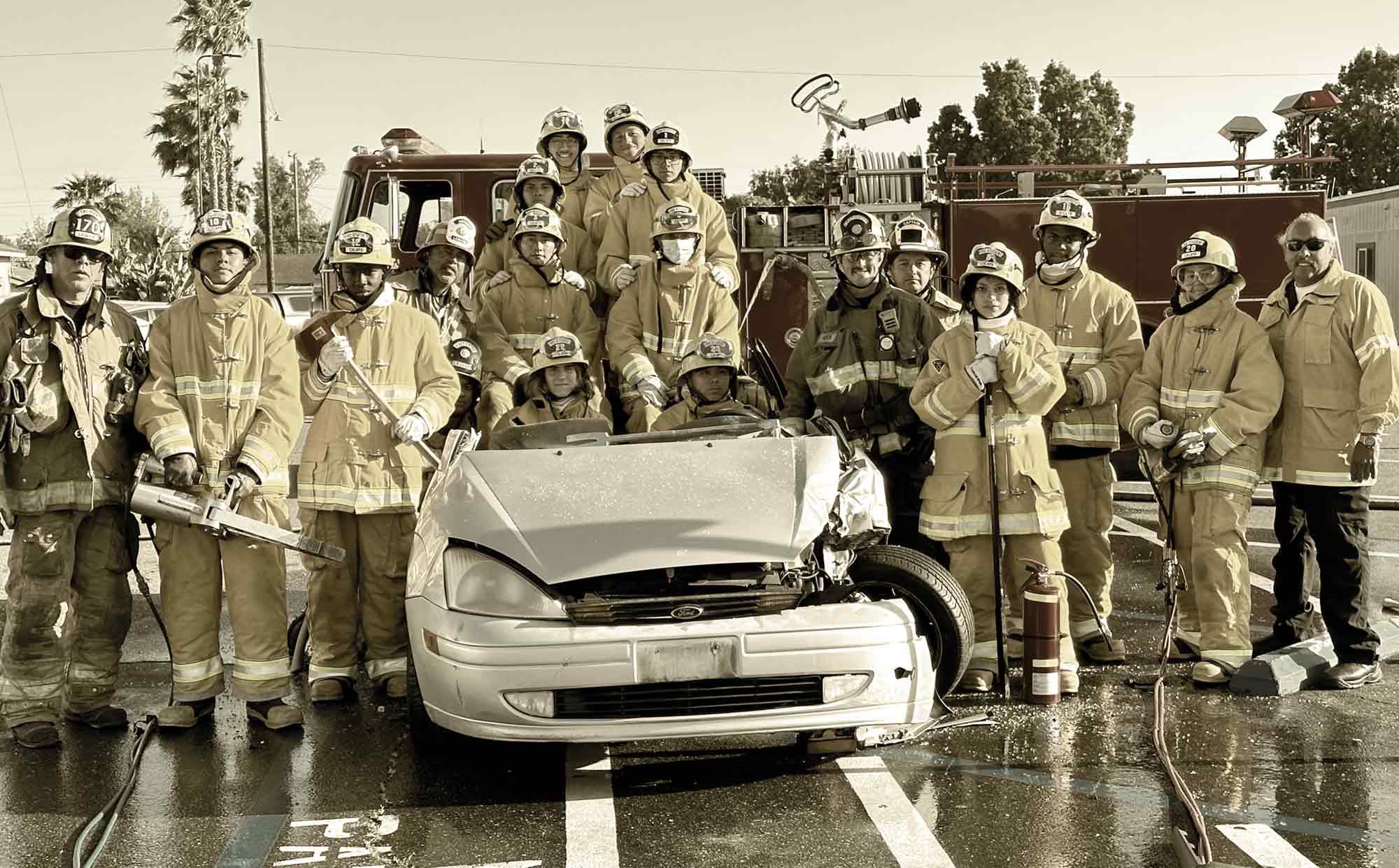 Advanced Pathways firefighters posing for a photo next to a wrecked car