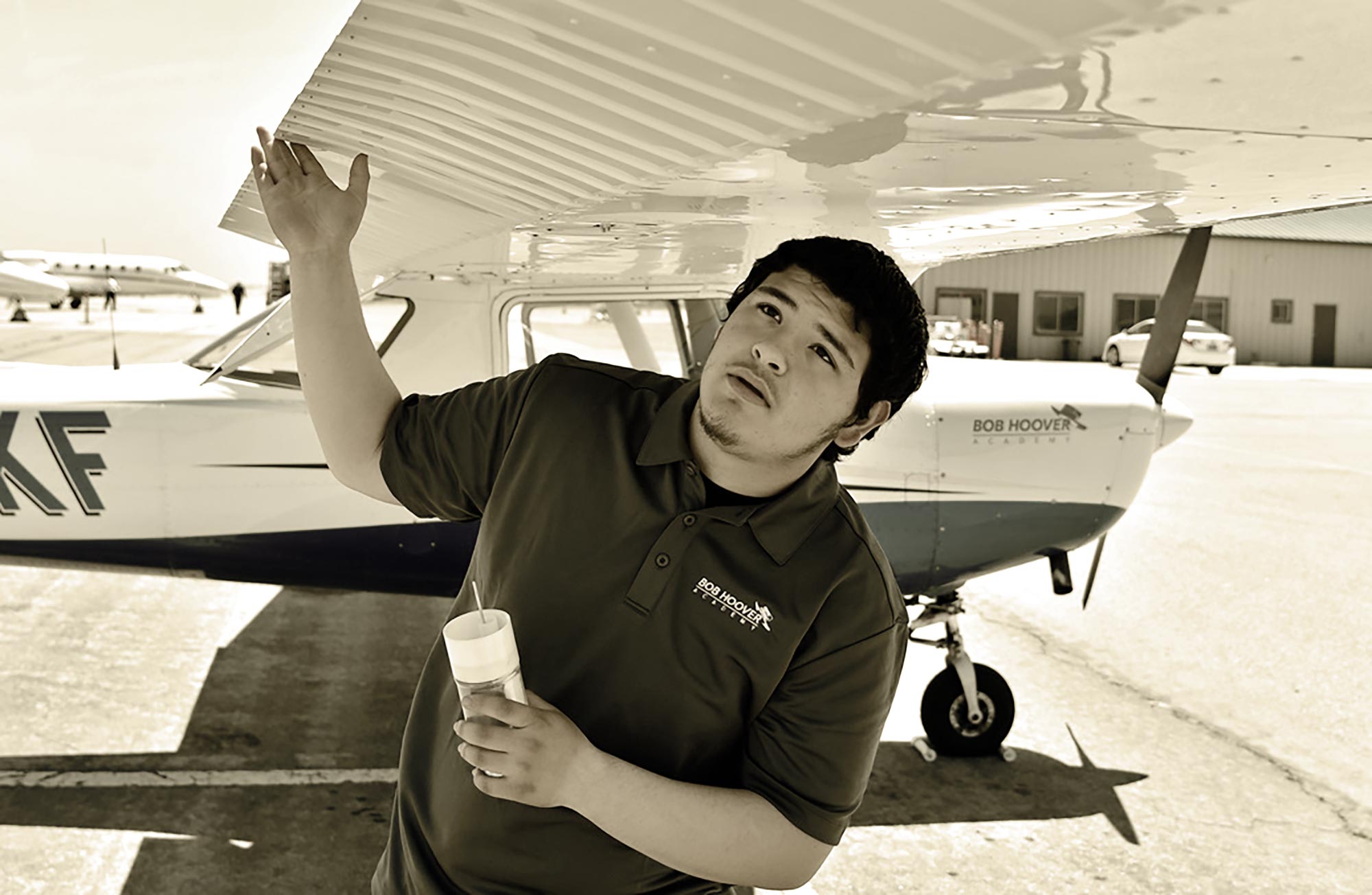 a male student wearing a Bob Hoover Academy embroidered polo shirt examines the wing of a small plane parked on a tarmac