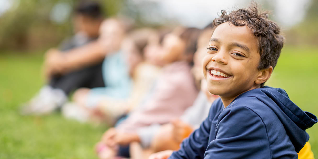 a little boy smiling while sitting in a line with his class mates