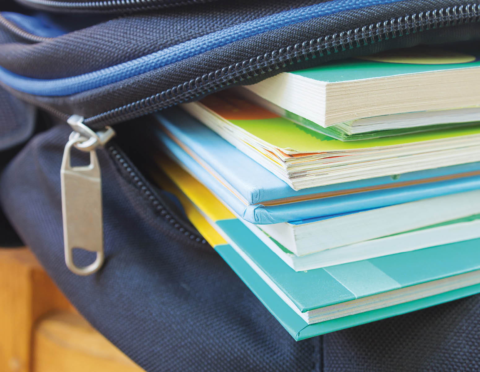 close up of yellow, green, and blue books sticking out of a blue backpack