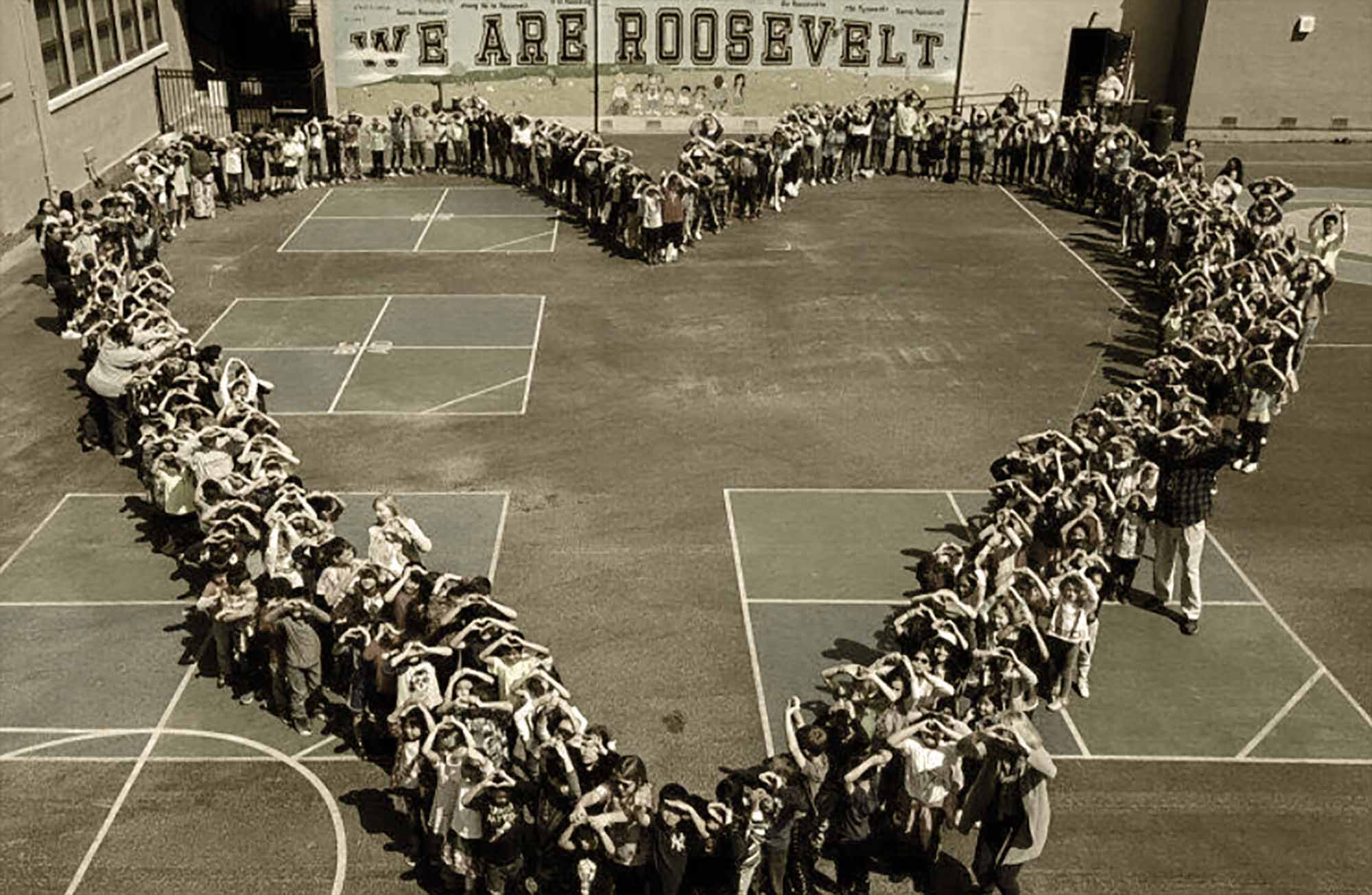 Landscape aerial photograph perspective of the Roosevelt Elementary School students standing outside with the teachers forming a heart shaped gesture in the blacktop area