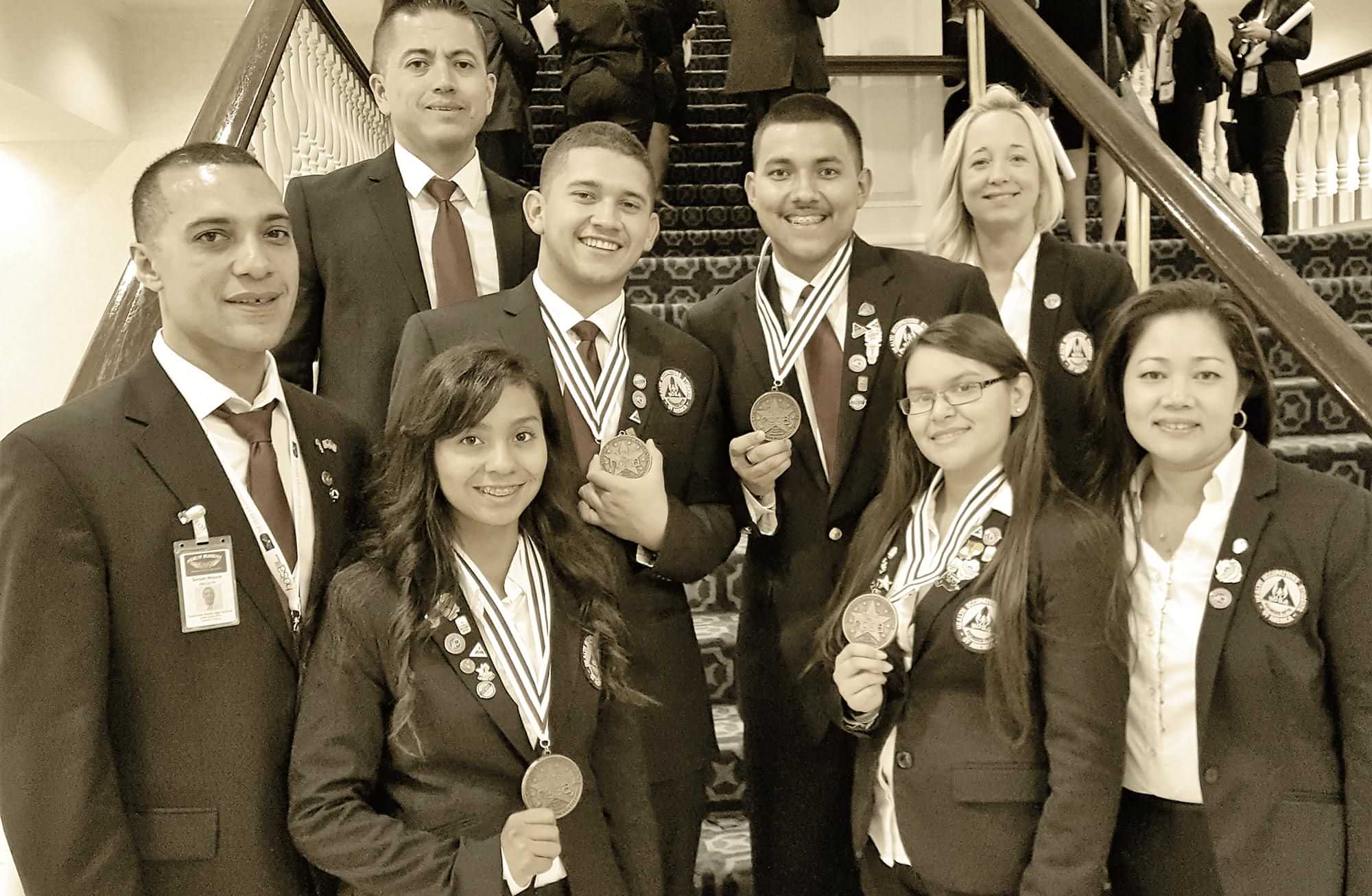 student members of the Academies of Coachella Valley High School stand on a staircase for a group photo and displaying medal awards