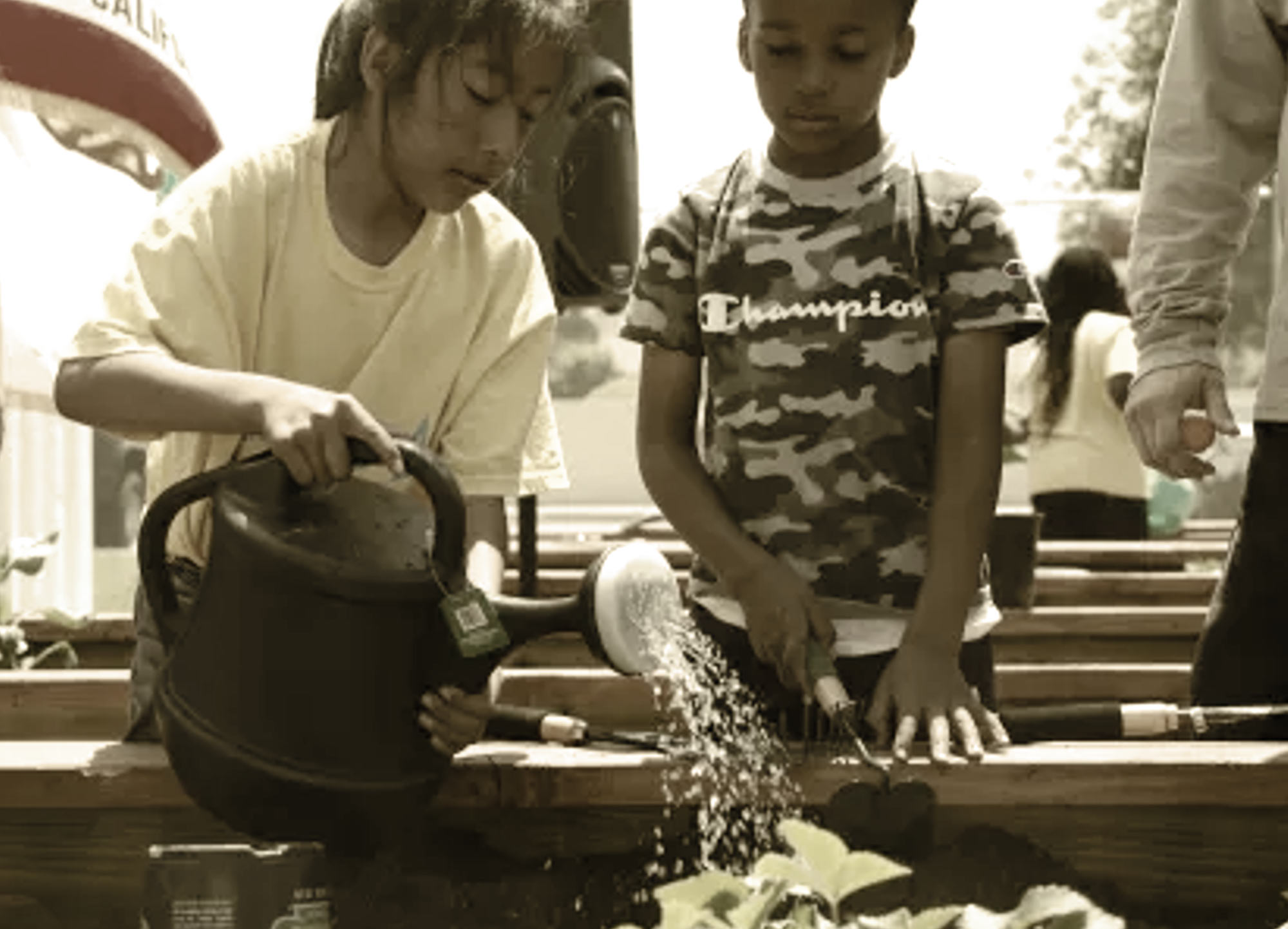 two elementary aged children water and tend to plants in an outdoor garden