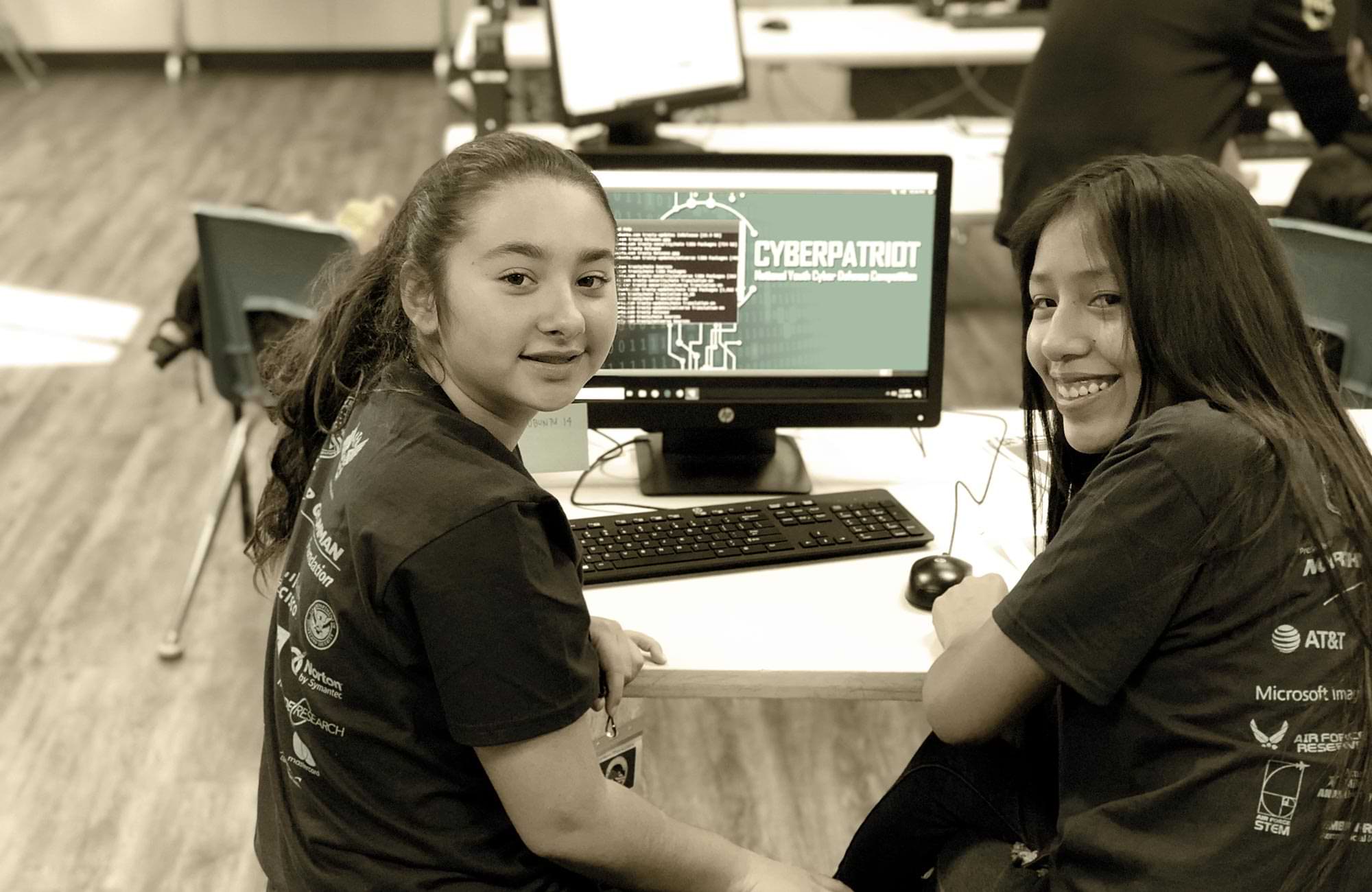 two young female students pause for a picture while working at a computer as part of the Los Nietos Middle School STEAM Academy Cybersecurity Program