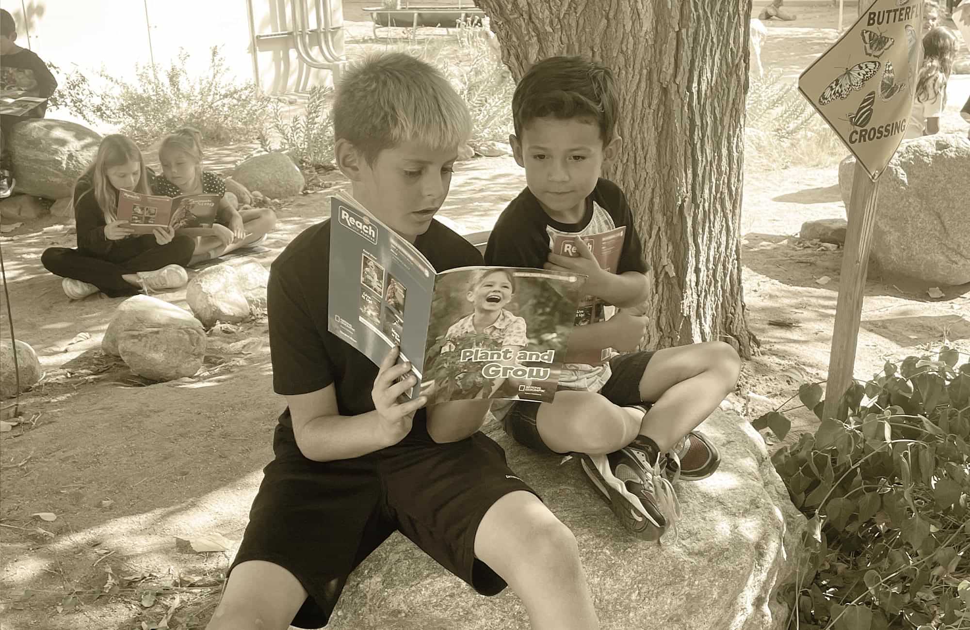 two couples of elementary aged students sit on rocks outside while reading together