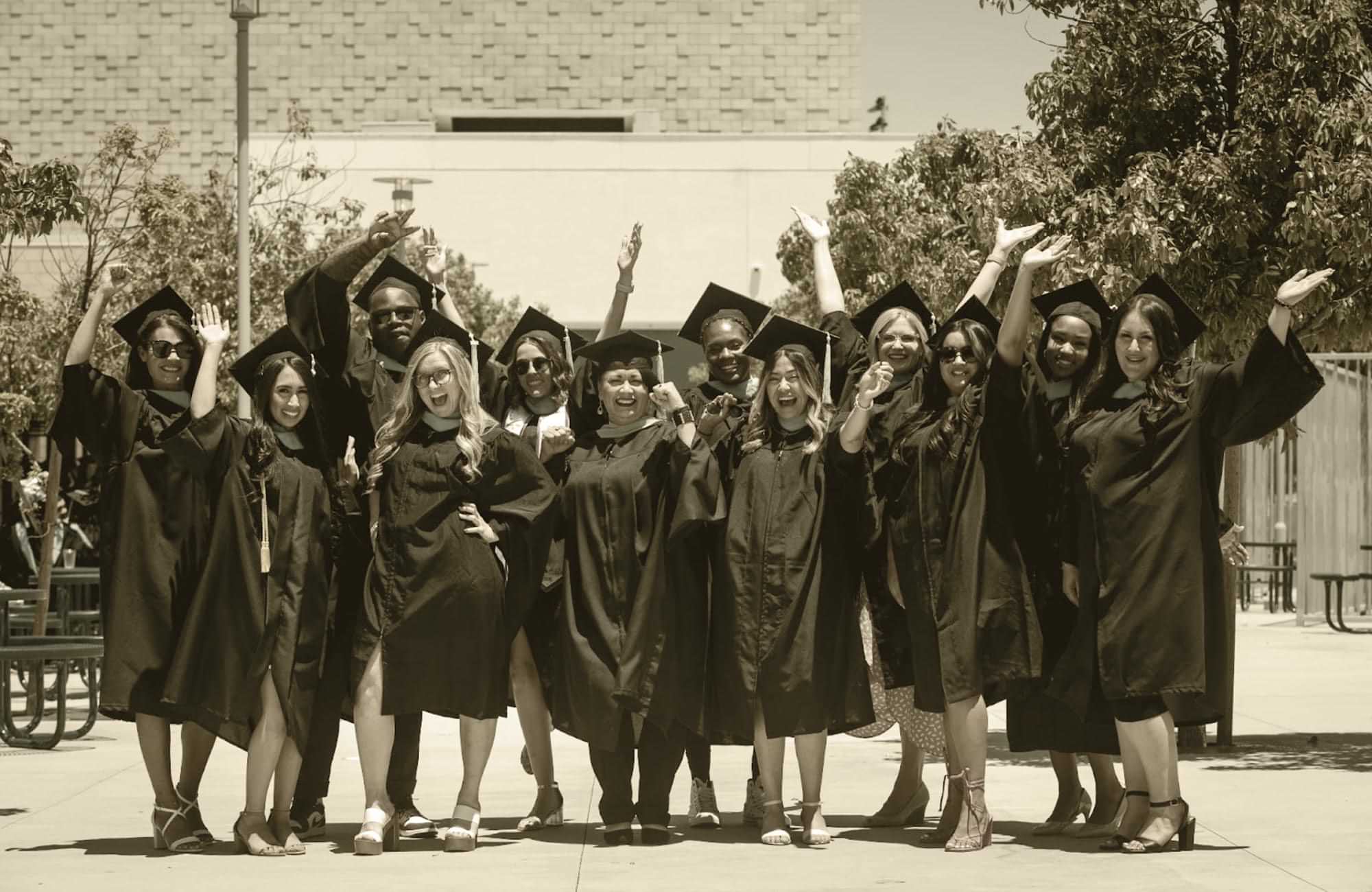 adult graduates pictured wearing robes and caps and standing together in celebration 