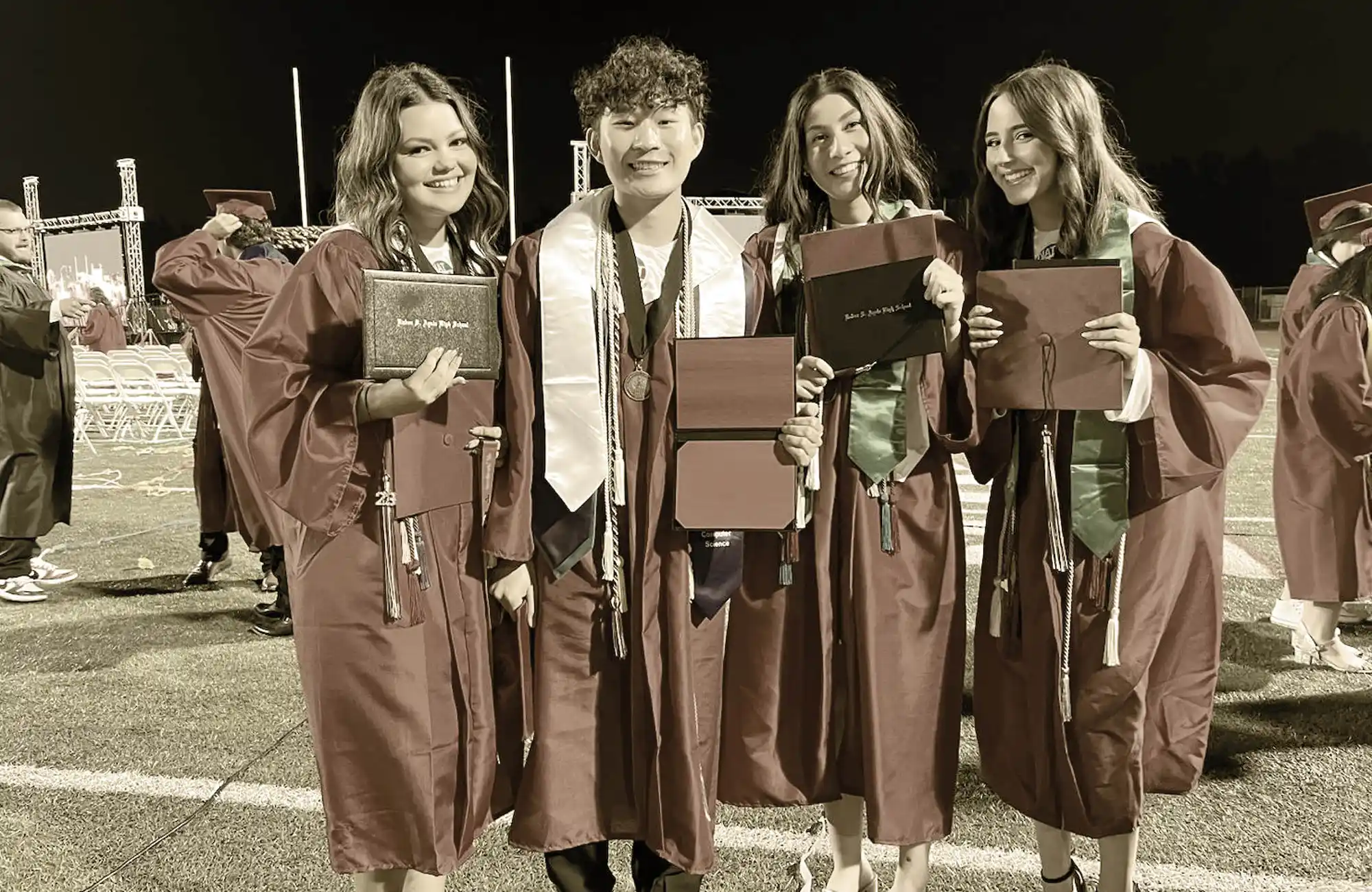 four students smile with their diplomas at their graduation ceremony