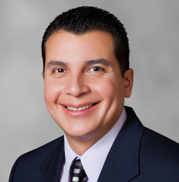President's Albert Gonzalez's headshot, wearing a dark blue suit jacket and a button up shirt and tie